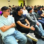 Audience attentively listens during a community event in a classroom setting.