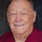 Elderly man smiling in red shirt against a dark background. Portrait photo.