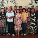 Large family gathering smiles in colorful outfits under musical note decor.